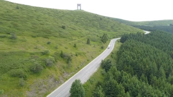 Widok z lotu ptaka na białą przyczepę kempingową lub furgonetkę towarową jadącą górską autostradą przed pięknymi zielonymi wzgórzami — Wideo stockowe