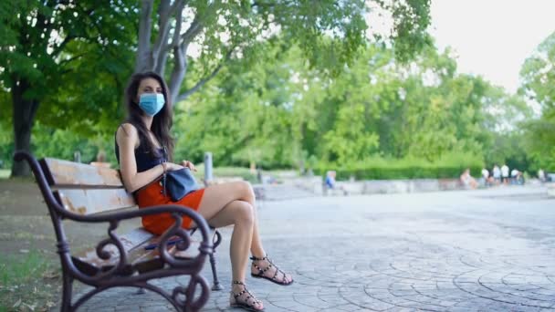 Mulher morena usando máscara protetora no parque. Distanciamento social no público — Vídeo de Stock