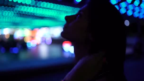 Jonge vrouw kijkt 's nachts naar de lichten in pretpark — Stockvideo