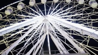 Aydınlatılmış dönme dolabın gece boyunca parlayan beyaz ışıkları olan alt manzarası.