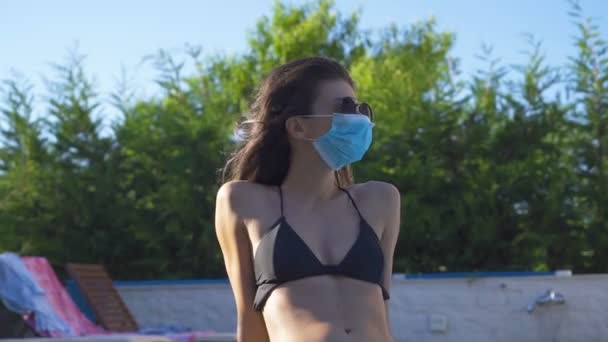 Mujer en bikini con máscara facial y gafas de sol mirando hacia arriba, soñando despierto. Distanciamiento social durante la pandemia de COVID-19 — Vídeo de stock