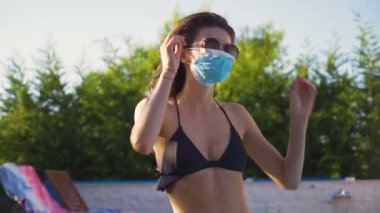Siyah bikinili ve maskeli genç bir kadın güneş gözlüğünü takıyor.