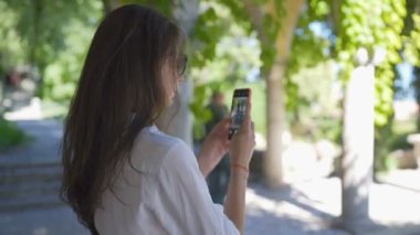 Turist kadın akıllı telefonuyla güzel yeşil park ve eski binaların fotoğraflarını çekiyor.
