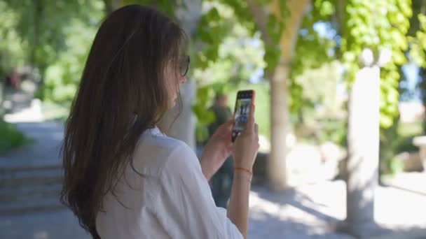 Wanita turis mengambil foto taman hijau yang indah dan bangunan kuno menggunakan smartphone-nya — Stok Video