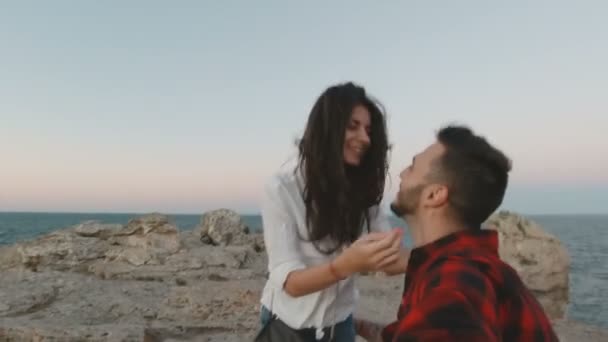 Fiatal pár mosolyog, ölelkeznek és filmezik magukat a part szélén, tengeri horizonttal a háttérben — Stock videók