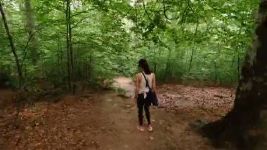 Genç bir kadın dağ ormanında bir patikada yürürken etrafına bakıyor. Hiperlapse
