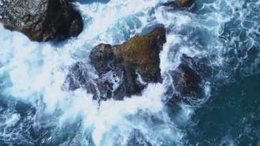 Şiddetli mavi deniz dalgaları Karadeniz kıyısındaki büyük ıslak kayaların üzerinde kırılıyor.