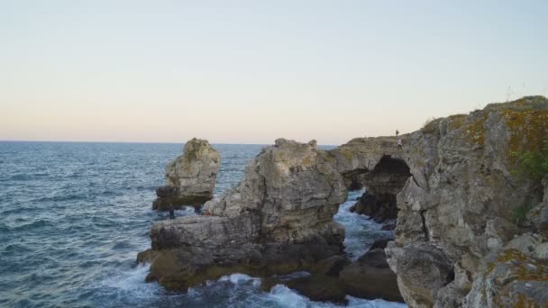 Vue aérienne des touristes marchant sur l'arc rocheux dans la mer près de Tyulenovo dans la journée ensoleillée d'été — Video