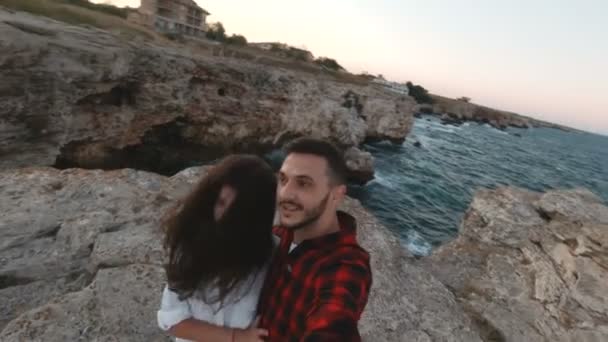 Mulher bonita com cabelo soprado pelo vento beijando seu namorado na costa do mar com ondas batendo no fundo — Vídeo de Stock
