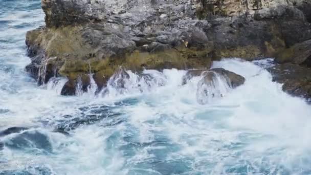 검은 해 안에 있는 거대하고 습한 바위 위로 굽이치는 청록색 파도 — 비디오