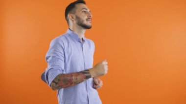 Tişörtlü genç adam turuncu duvar arkasında dans ediyor. Mutlu, pozitif erkek dans konsepti