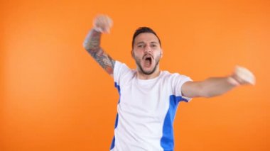 Genç hevesli futbol fanatiği kaleyi kutluyor. Kollarını kaldırıyor, turuncu arka planda izole halde.