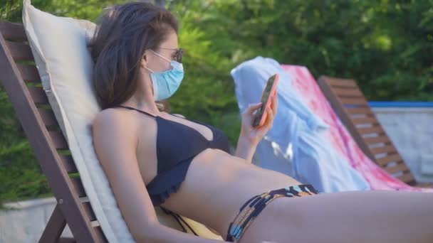 Mulher de biquíni usando máscara facial passando o dia ao redor da piscina — Vídeo de Stock