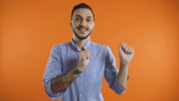 Jovem sorrindo homem de camisa fazendo vencedor dança feliz, apresentando para o lado com ambos os braços — Vídeo de Stock