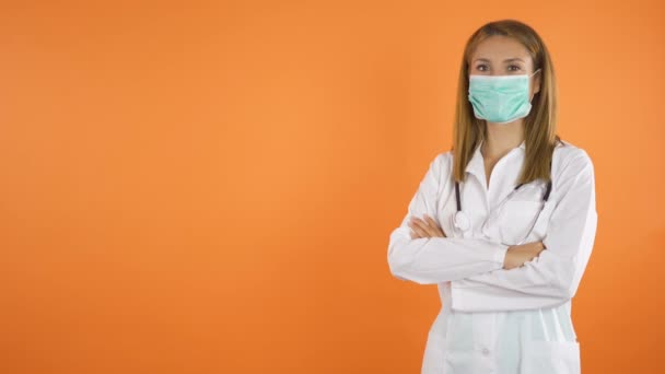 カメラの前で顔のマスクの笑顔を持つ女性医師。オレンジスタジオの背景コピースペースコンセプト — ストック動画