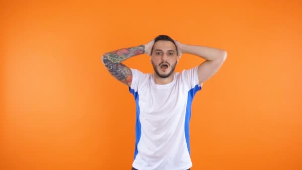Trauriger schreiender emotionaler Mann Fan in weißblauem T-Shirt steht isoliert vor orangefarbenem Hintergrund — Stockvideo