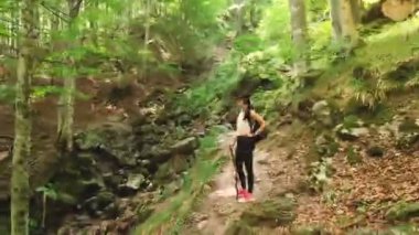 Spor giyimli genç bir kadının ormanda yürüyüşünü, kayalık arazide yürüyüşünü izlemek.