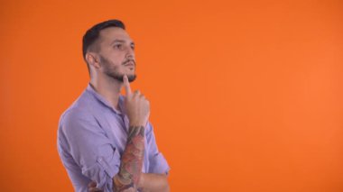 Düşünceli bir adam, yüzü parmaklarıyla düşünüyor, turuncu arka planda soyutlanmış..