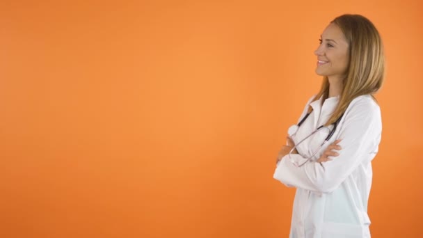 Schöne Ärztin oder Krankenschwester im weißen Mantel vor orangefarbenem Hintergrund, Studioaufnahme. Konzept präsentieren, reden — Stockvideo