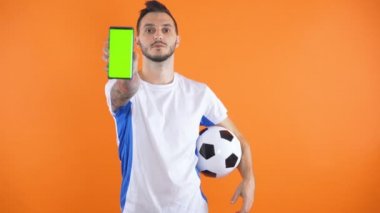 Futbol fanatiği beyaz mavi gömlekli yeşil ekran turuncu arka plan gösteriyor 