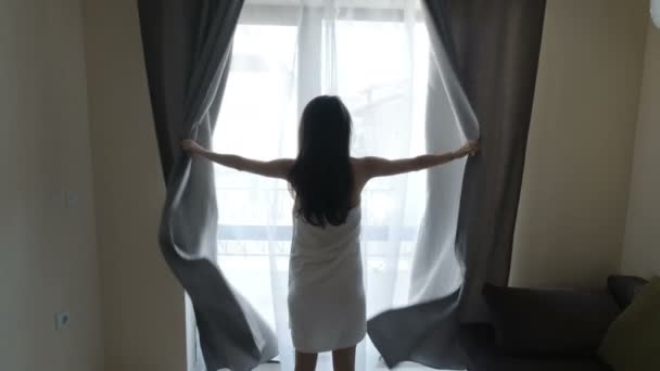 Beautiful fit woman wearing only a towel pulls curtains in the morning — Stock Video