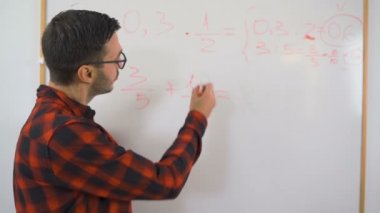 Kırmızı gömlekli ve gözlüklü genç öğretmen uzaktan matematik öğretiyor. 