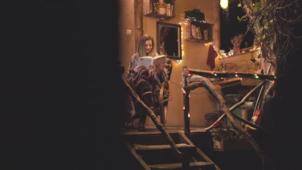 Těhotná žena číst knihu a houpačky v křesle před malým útulným domem na Vánoce — Stock video