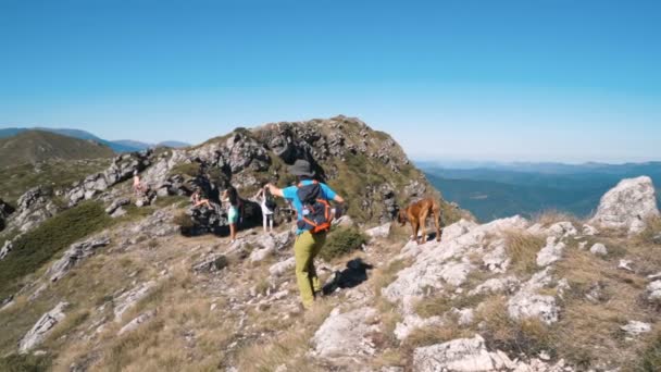 Grupo de mochileiros caminhando em montanhas em cume rochoso. Jovem apontando para a frente com a mão — Vídeo de Stock