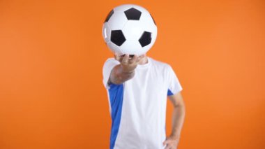 Futbol fanatiği, beyaz mavi gömlekli, tek eliyle topu suratının önünde tutuyor.