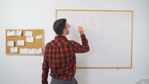 Genç erkek matematik öğretmeni beyaz tahtaya matematiksel denklemler yazıyor. Çevrimiçi sınıf ve e-öğrenim öğretmeni için kırmızı işaret kullanıyor. — Stok video