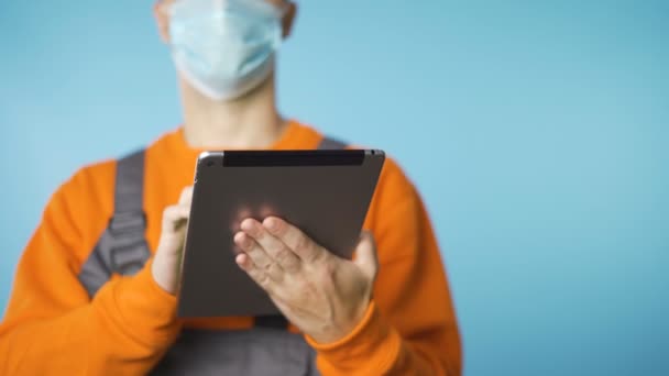 Nahaufnahme eines männlichen Handwerkers mit Gesichtsmaske bei der Arbeit am Tablet isoliert auf blauem Hintergrund — Stockvideo