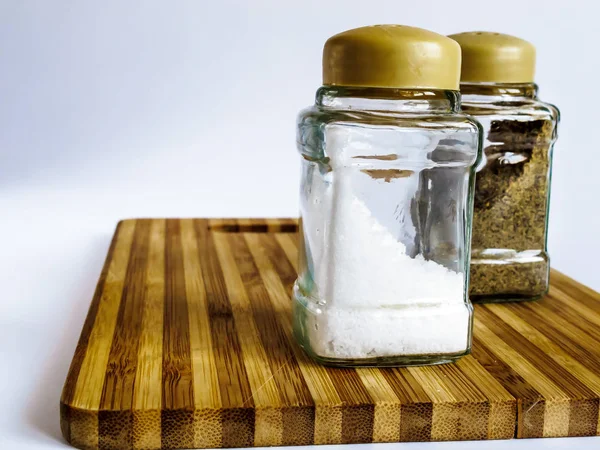 Salt and pepper in a glass shaker and pepper shaker stand on a cutting board