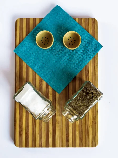 Salt and pepper in a glass shaker and pepper shaker stand on a cutting board