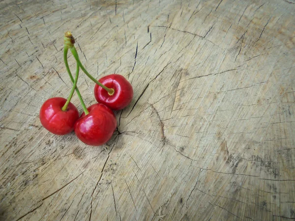 Három vörös édes cseresznye feküdni egy fa vágott — Stock Fotó