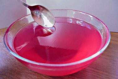 cam bir kase ve üstüne küçük bir kaşık kırmızı jöle