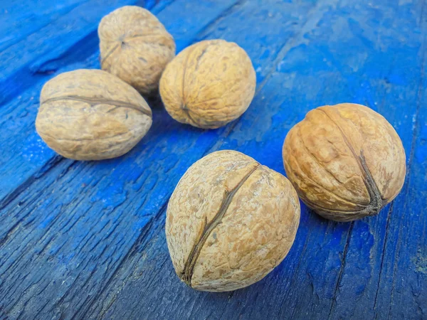 Vijf rijpe walnoten liggen op een blauwe houten achtergrond. Selectieve focus op twee moeren. de rest van de moeren in de onscherpe — Stockfoto