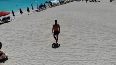 Genç bir erkek model yavaş çekimde beyaz kumlu Karayipler sahilinde yürür Genç bir erkek model beyaz kumlu Karayip ler plajında yavaş çekimde turkuaz suya doğru yürür.