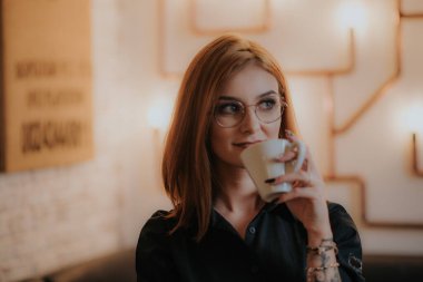  Gözlüklü genç kadın kahve içiyor.