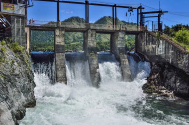 Chemal Köyü, Altay Cumhuriyeti, Rusya Federasyonu - 7 Temmuz 2018: Chemal Nehri (Altay Dağları), eski hidroelektrik santrali. Köprü, baraj, şelaleler, su yaz güneşli manzara, köpük akışı görünümü 