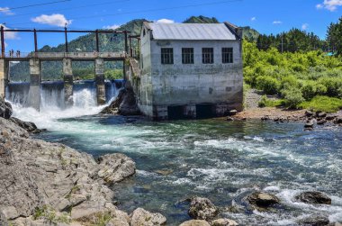 Chemal Köyü, Altay Cumhuriyeti, Rusya Federasyonu - 7 Temmuz 2018: Chemal Nehri (Altay Dağları), eski hidroelektrik santrali. Köprü, baraj, şelaleler, su yaz güneşli manzara, köpük akışı görünümü