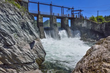 Chemal Köyü, Altay Cumhuriyeti, Rusya Federasyonu - 7 Temmuz 2018: Chemal Nehri (Altay Dağları), eski hidroelektrik santrali. Köprü, baraj, şelaleler, su yaz güneşli manzara, köpük akışı görünümü