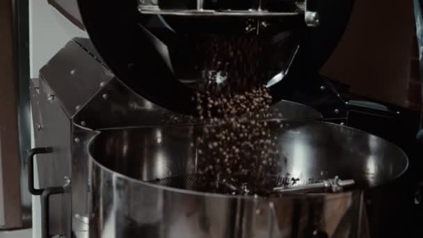 ある男がコーヒー製造機を操作している 彼は鉄の容器を開け 茶色の焙煎コーヒー豆が回転ホイールで大きなスチールボウルに落ちている — ストック動画