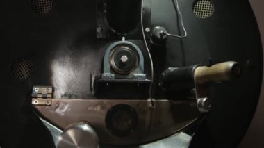 Ahşap ve demir saplı kahve yapma makinesi. Ekipmanlar çalışıyor. Kahverengi kavrulmuş kahve çekirdekleri kahve makinesi aroung dönüyor. Kamera sağa doğru hareket ediyor..