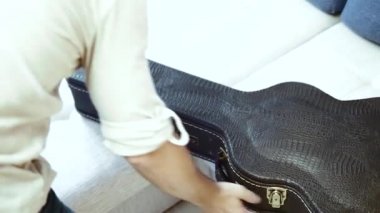 Bir gitarist siyah deri bir çanta açıyor ve akustik gitarı çıkarıyor..