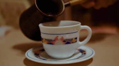 Sıcak kahverengi koyu kahve yuvarlak bir fincan üzerinde beyaz bir fincana dökülüyor. Meyve suyu bardağın üzerinden akıyor ve masanın yüzeyinde akıyor..