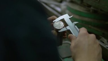 Bir fabrika işçisinin elleri metal bir detay ve kaydırak göstergesi tutuyor. İşçi ayrıntıları ölçmek için el kalibrelerini kullanıyor. Sonra ayrıntıları ters çevirip tekrar ölçüyor..