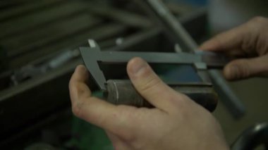 Bir fabrika işçisinin elleri metal bir detay ve kaydırak göstergesi tutuyor. İşçi ayrıntıları ölçmek için el kalibrelerini kullanıyor. Sonra kalibreli tabancayı masaya geri koydu..
