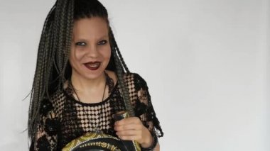 Uzun gri afro örgülü, koyu renk makyajlı gotik bir kız bir didjeridu 'ya bakıyor ve gülüyor. Müzik malzemeleri mağazası ya da müzik mağazası için yaratıcı bir konsept..