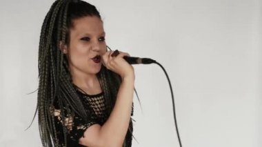 Uzun gri afro örgülü, koyu renk makyajlı gotik bir kız mikrofona şarkı söylüyor. O bir vokalist veya şarkıcı gibi davranıyor. Müzik malzemeleri mağazası ya da müzik mağazası için yaratıcı bir konsept..