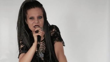 Uzun gri afro örgülü, koyu renk makyajlı gotik bir kız mikrofona şarkı söylüyor. O bir vokalist veya şarkıcı gibi davranıyor. Müzik mağazası için yaratıcı bir kavram ya da müzik teşvikleri.